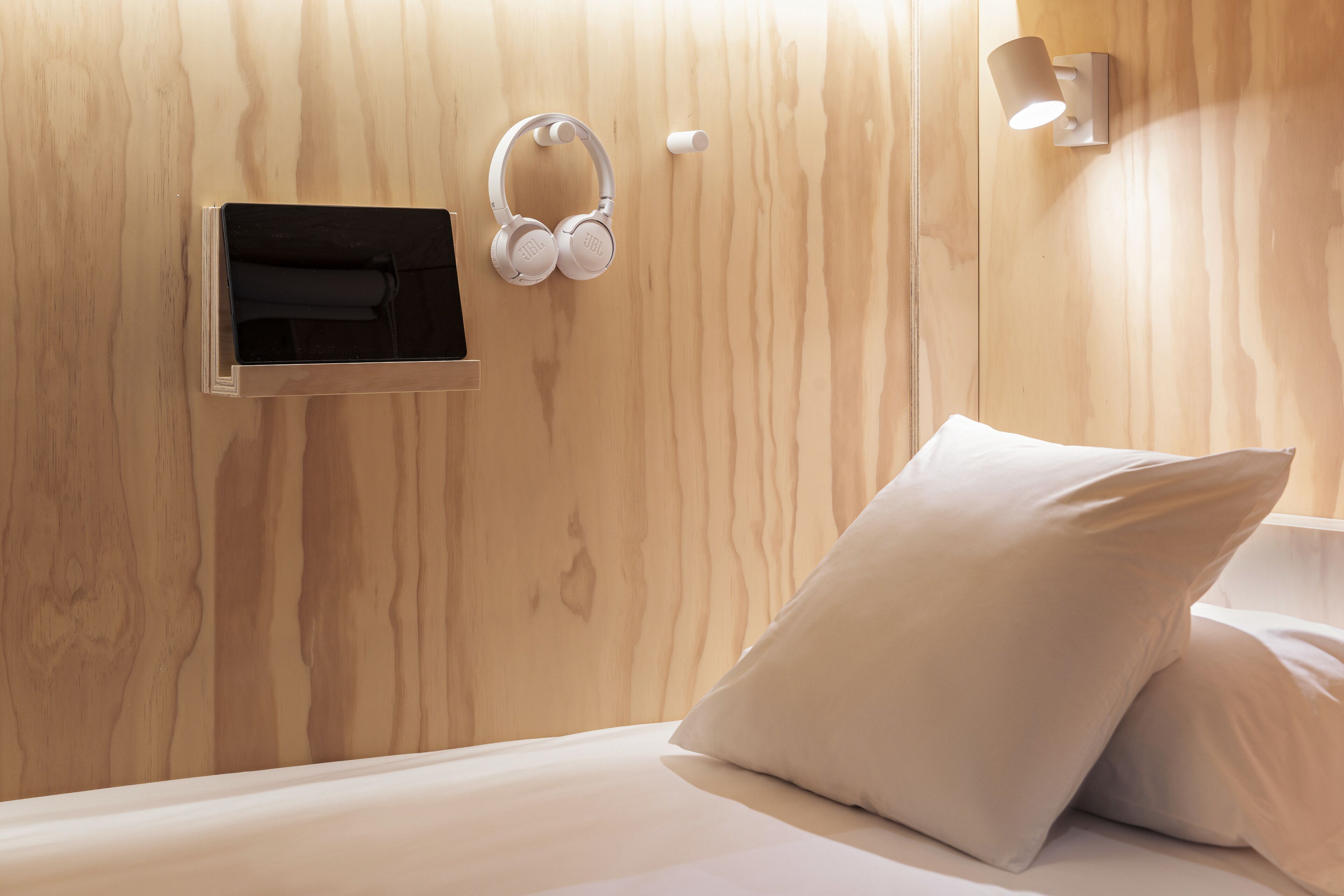Habitación de hotel con pared de madera, cama con ropa blanca, almohada y un par de auriculares colgados en la pared.