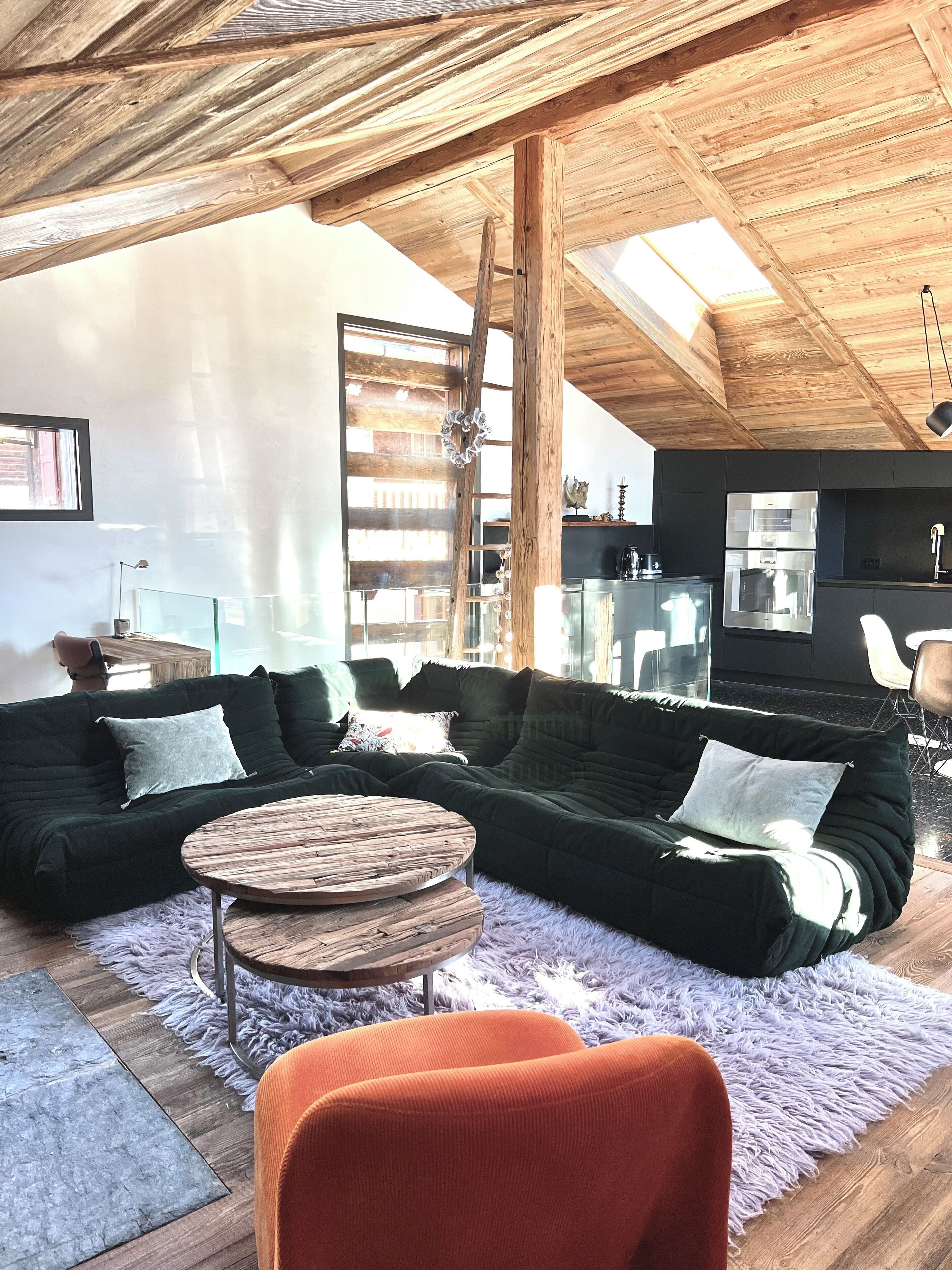 Ein modernes Wohnzimmer mit einem Ecksofa, einem runden Holztisch und einem flauschigen Teppich.