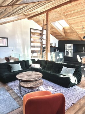 Uma sala de estar moderna com um sofá seccional, uma mesa de centro redonda de madeira e um tapete felpudo.