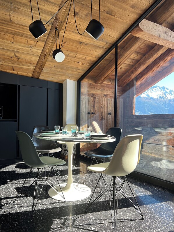 Uma sala de jantar moderna com uma mesa redonda, quatro cadeiras e iluminação pendente.