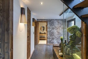 Um corredor moderno com porta de madeira, luminária na parede, parede com padrão e porta de vidro que dá para um banheiro.
