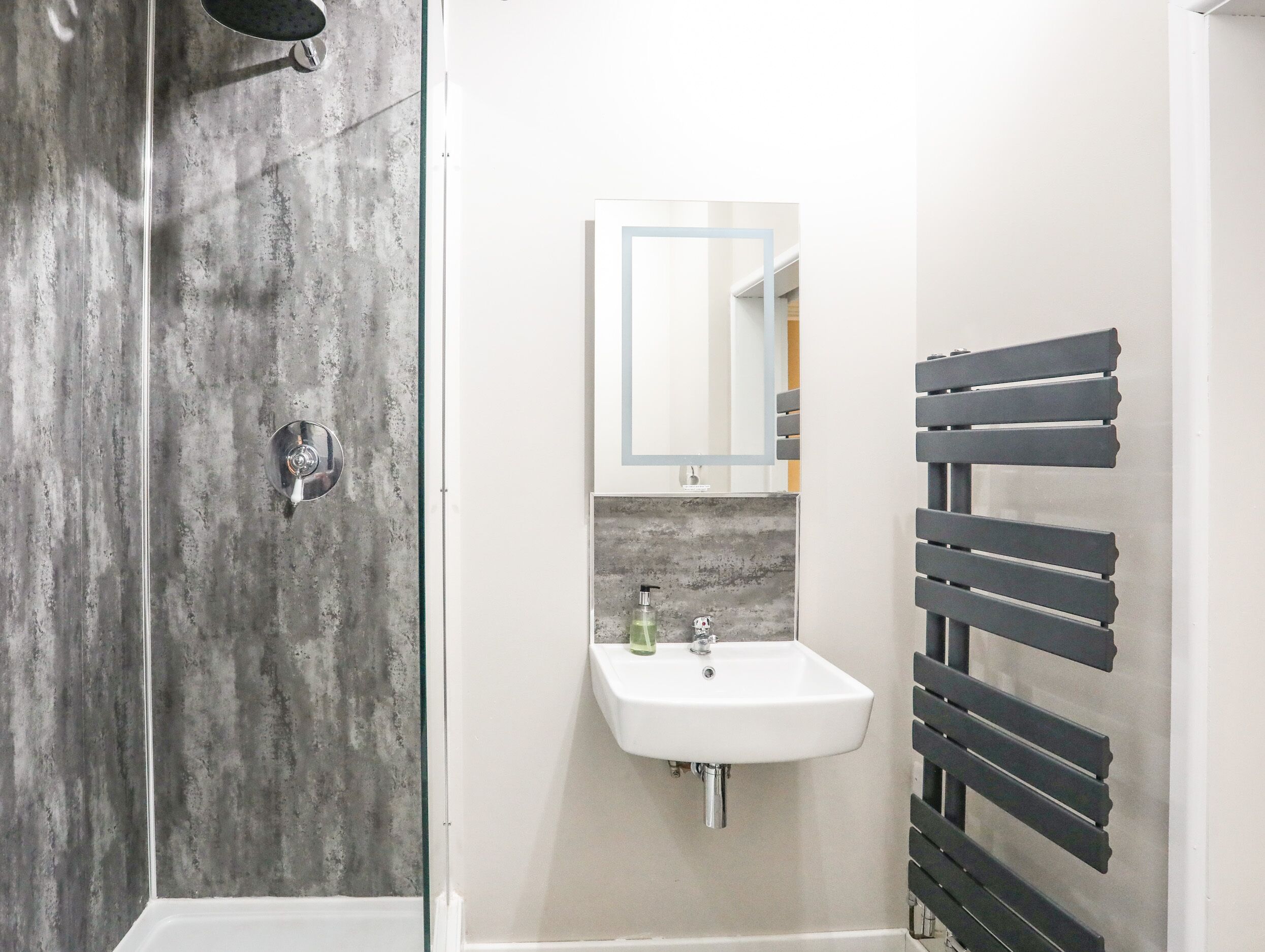 A modern bathroom with a glass shower enclosure, a white sink with a mirror above it, and a black towel rack.