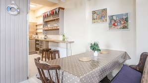 A dining area with a table set for four, wooden chairs, a bench, and a wall-mounted bar with shelves of glasses. - No 62 (Beaumaris)