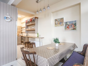 A dining area with a table set for four, wooden chairs, a bench, and a wall-mounted bar with shelves of glasses.