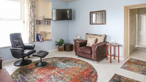 A living room with a sofa, a chair, a coffee table, a TV, a bookshelf, and a patterned rug. - No 62 (Beaumaris)