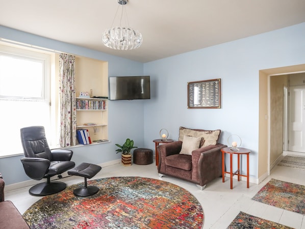 A living room with a sofa, a chair, a coffee table, a TV, a bookshelf, and a patterned rug.
