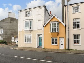 Une rangée de maisons mitoyennes aux styles architecturaux distincts, dont une maison jaune dotée d’une baie vitrée et une maison blanche avec un lucarne.