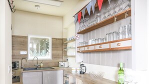 A modern kitchen with a built-in dishwasher, a window with a view, and a countertop with a coffee maker and glasses. - No 62 (Beaumaris)