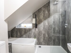 Une salle de bain moderne avec une baignoire, une cabine de douche en verre et une petite fenêtre où est posée une bougie.