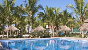 A swimming pool with palm trees and thatched umbrellas. - CONDOMINIO GRAND MARINA by TRVL2HM (Nuevo Nayarit)