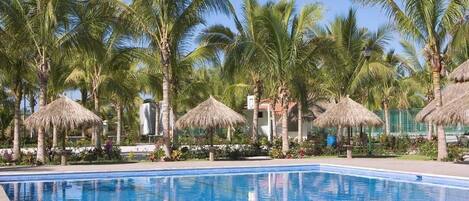 Piscina con palmeras y sombrillas de paja.