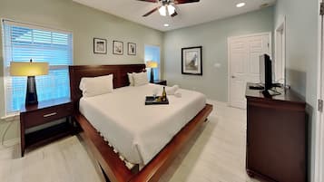 A hotel room with a bed, bedside lamps, a ceiling fan, a television, and framed pictures on the wall.