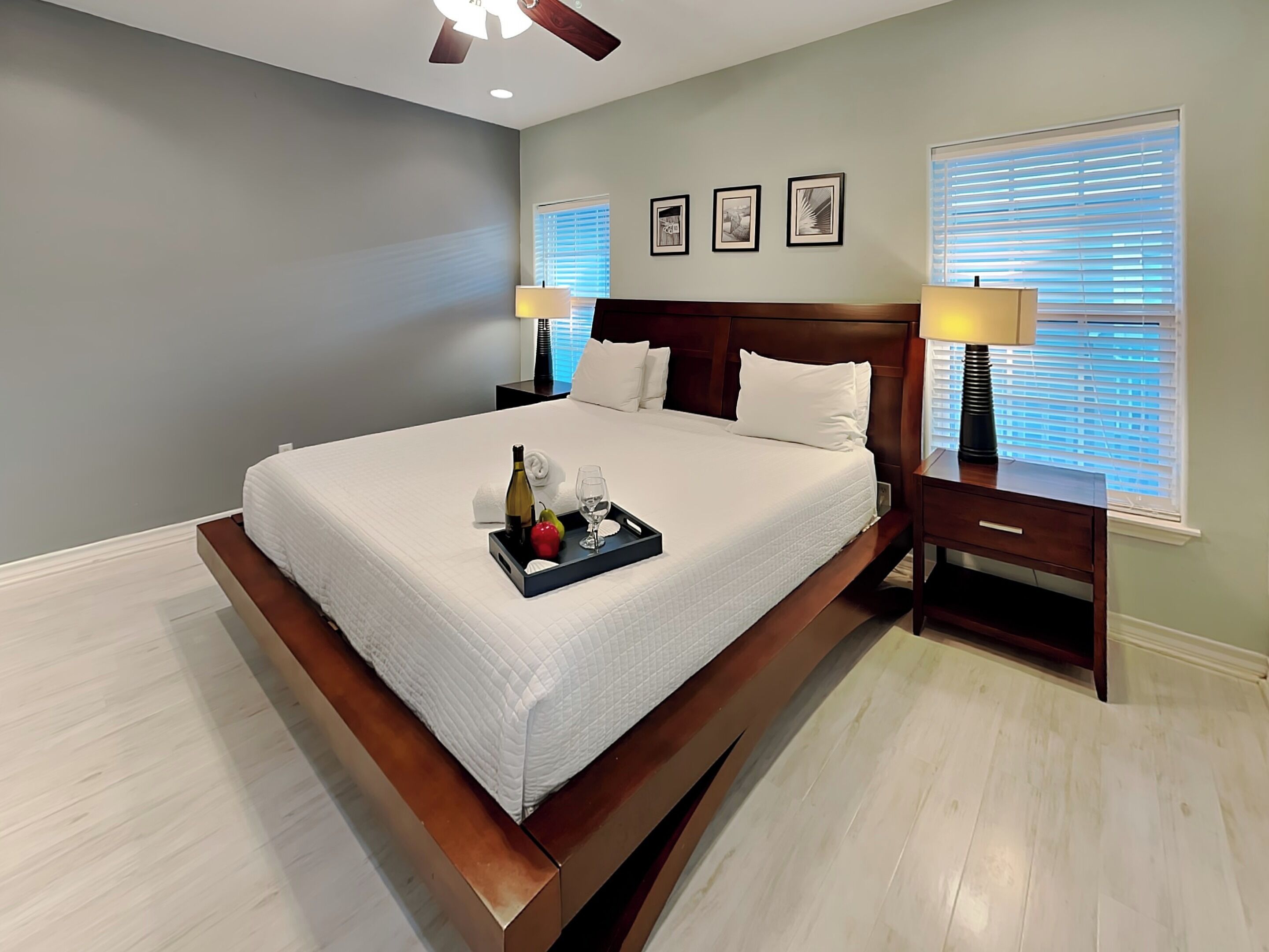 Une chambre d’hôtel avec un grand lit, une table de chevet avec une lampe, un ventilateur de plafond et des tableaux encadrés au mur.