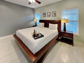 Una habitación de hotel con una cama grande, una mesita de noche con lámpara, un ventilador de techo y cuadros en la pared.