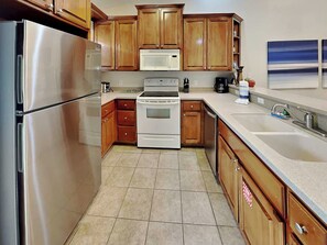 A kitchen with wooden cabinets, stainless steel appliances, a microwave, and a sink. - Beach Bunker by Silver Sands Vacation Rentals (Port Aransas)