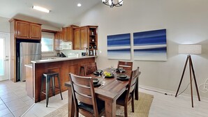 A modern kitchen with wooden cabinets, a stainless steel refrigerator, and a dining area with a wooden table and chairs. - Beach Bunker by Silver Sands Vacation Rentals (Port Aransas)