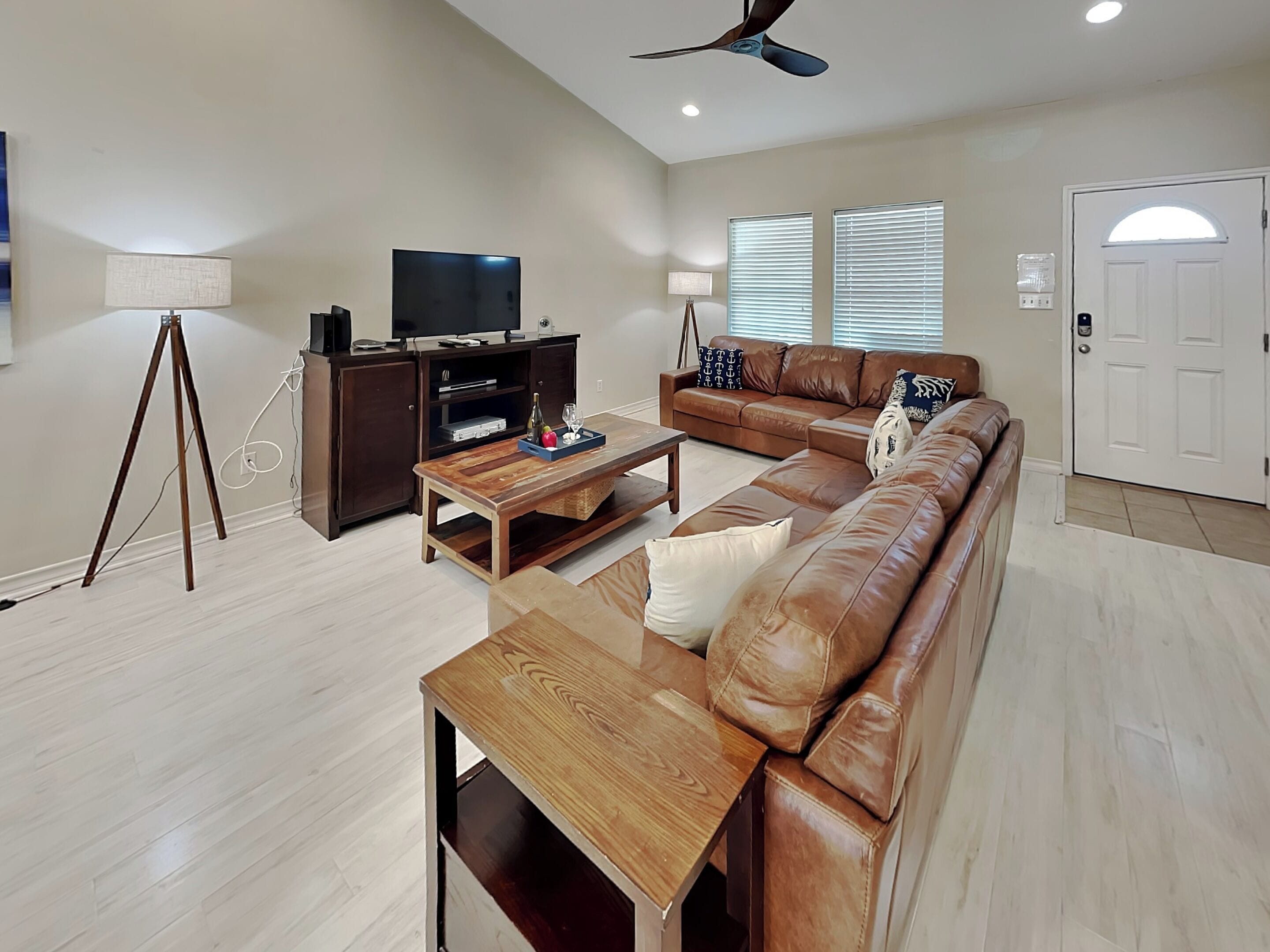 A living room with a sofa, coffee table, TV stand, and a ceiling fan.