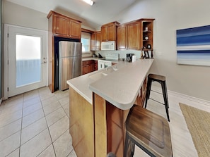 A kitchen with wooden cabinets, a stainless steel refrigerator, a microwave, and a large island with a sink.