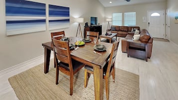 A dining area with a wooden table and chairs, a coffee table, and a sofa in the background.