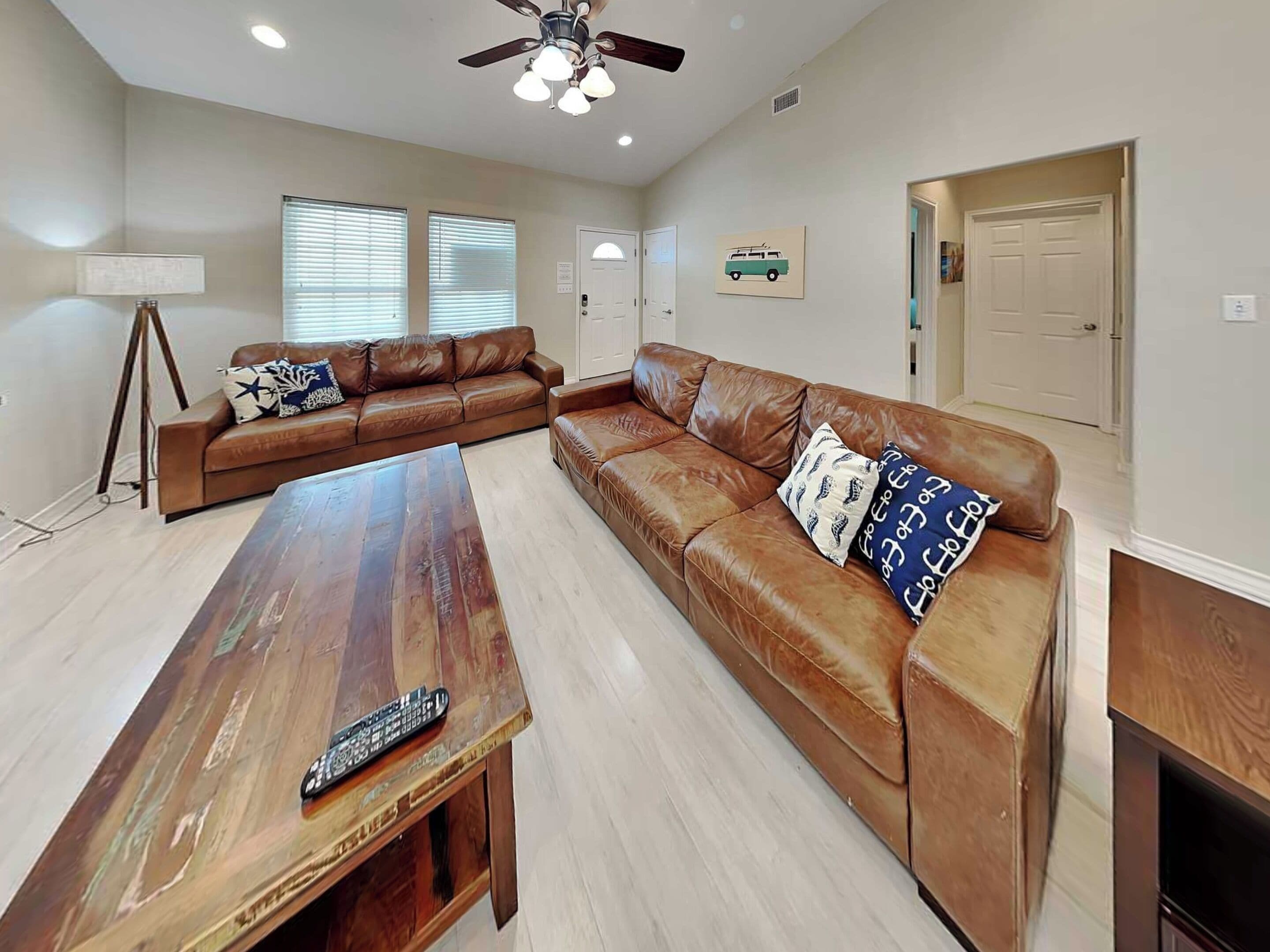 A living room with a brown leather sofa, a wooden coffee table, and a ceiling fan.