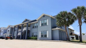 A multi-story residential building with a balcony on the second floor, a covered parking area, and palm trees in the foreground. - Beach Bunker by Silver Sands Vacation Rentals (Port Aransas)