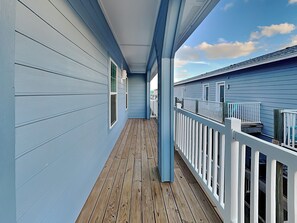 A covered wooden deck with a railing, light blue siding, and a clear sky. - Beach Bunker by Silver Sands Vacation Rentals (Port Aransas)