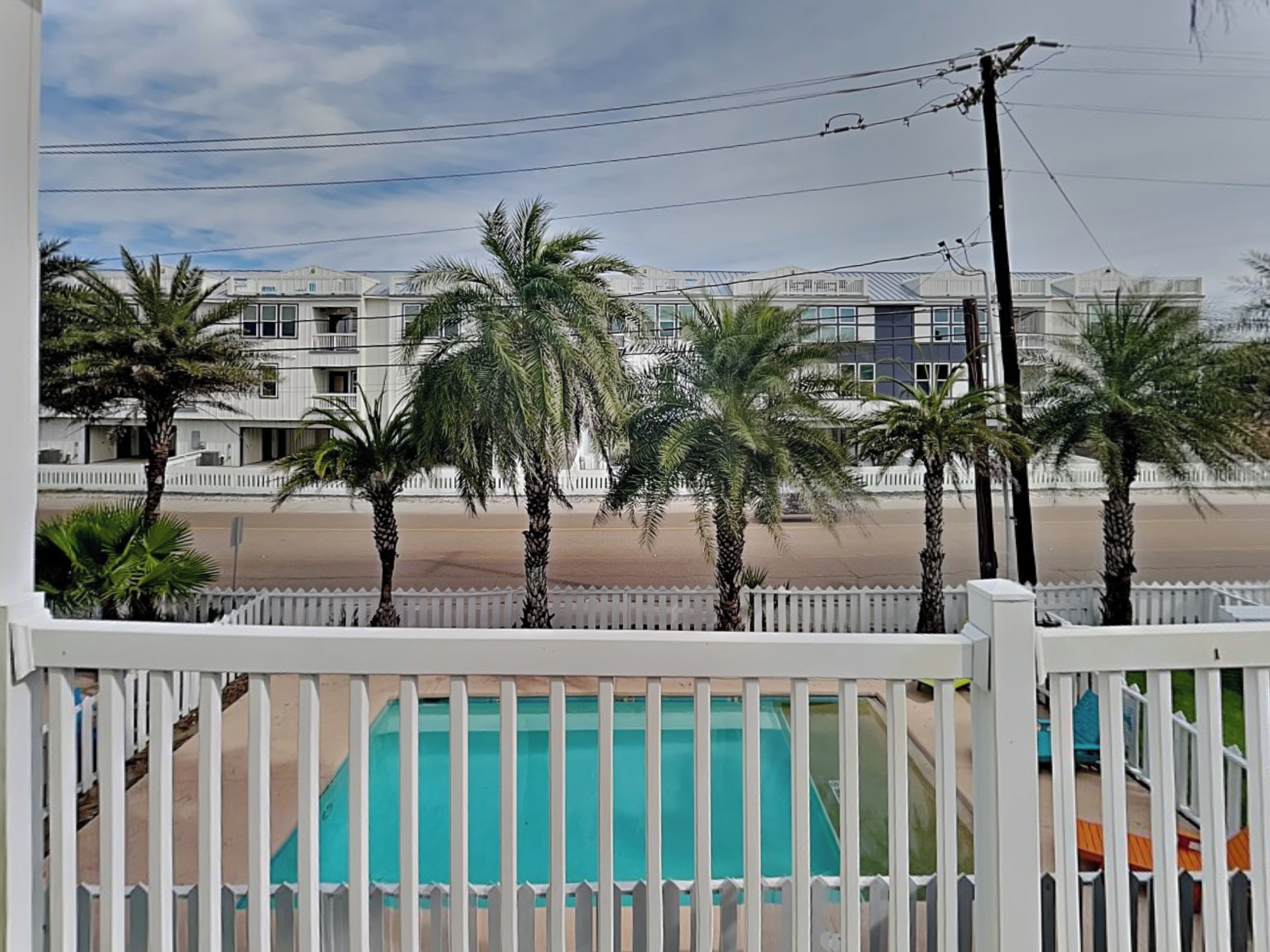 A pool area with a white fence, palm trees, and a view of buildings in the background.