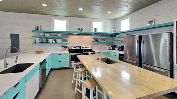 A modern kitchen with teal cabinetry, stainless steel appliances, and a central island with stools. - Beach Club 2 by Silver Sands Vacation Rentals (Port Aransas)