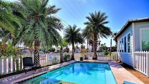 A swimming pool surrounded by palm trees and a white picket fence. - Beach Club 1 by Silver Sands Vacation Rentals (Port Aransas)
