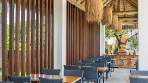 An outdoor dining area with wooden tables and chairs, a thatched roof, and a view of greenery. - Mikiki Lifestyle Hotel (Cajueiro da Praia)