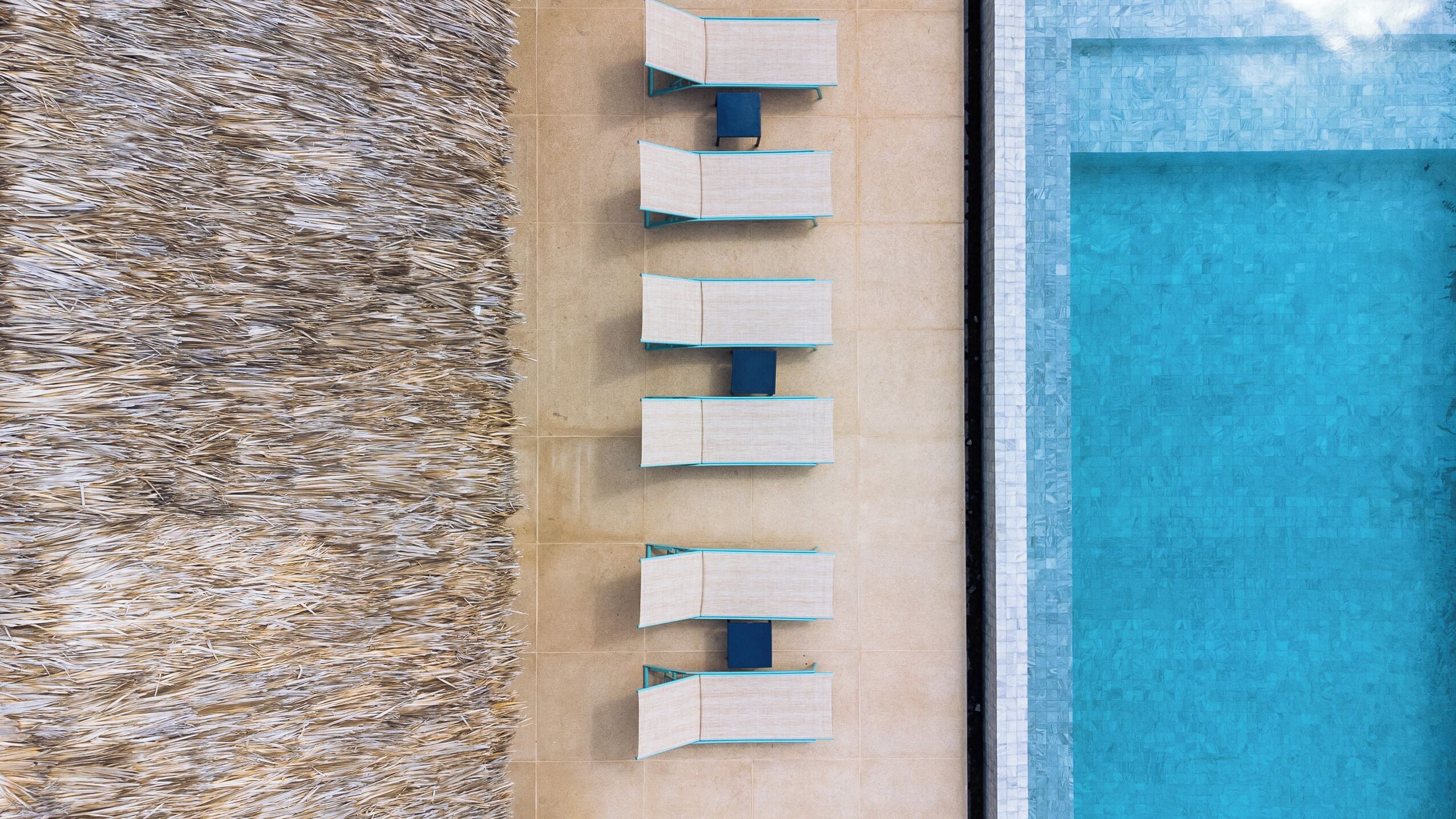 An aerial view of a pool area with a row of six blue lounge chairs and a tiled deck.