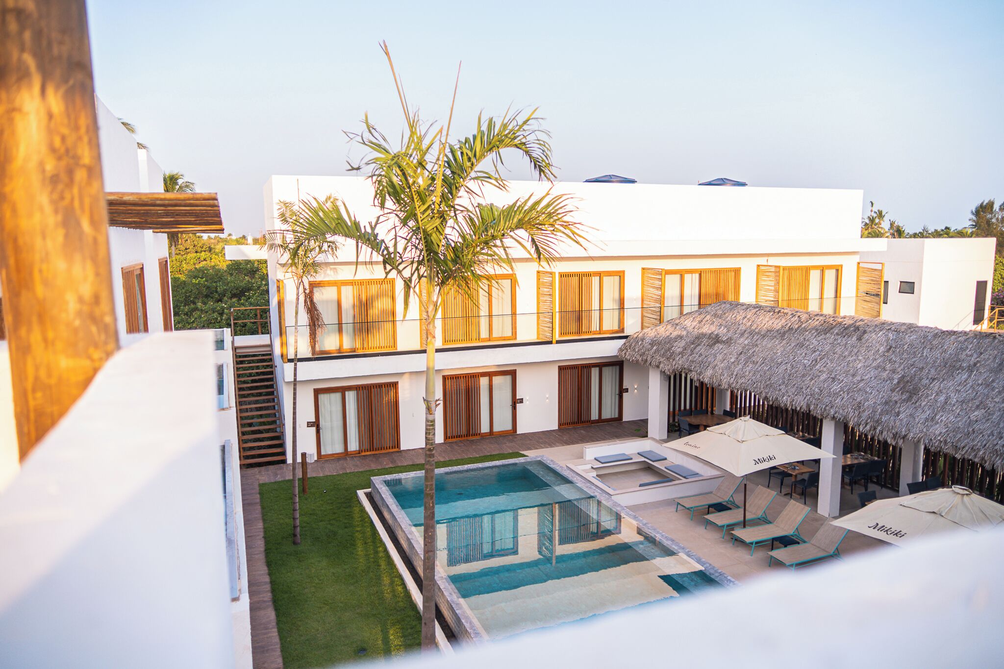 A modern house with a pool, outdoor seating, and a thatched roof.