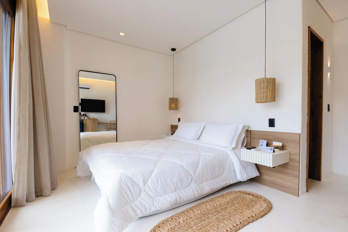 A modern bedroom with a large bed, a bedside table, a mounted TV, and a hanging light fixture.