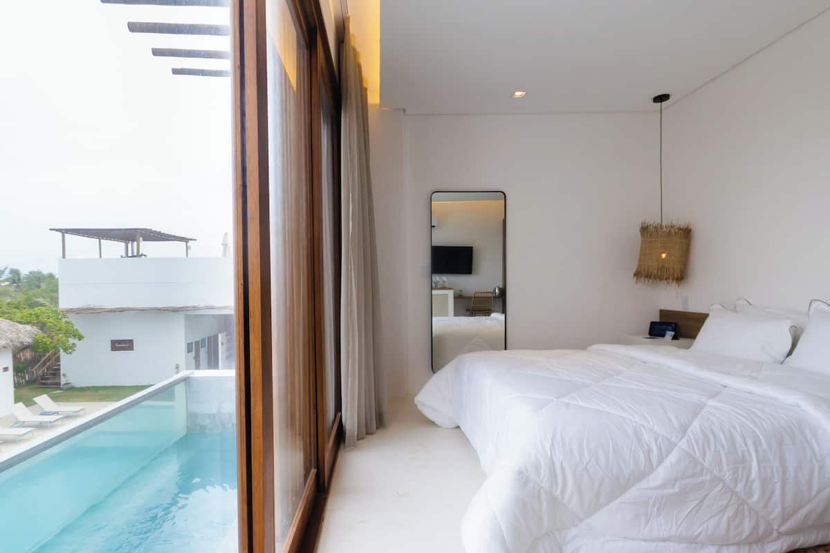 A modern bedroom with a large bed, a view of a swimming pool, and a balcony.