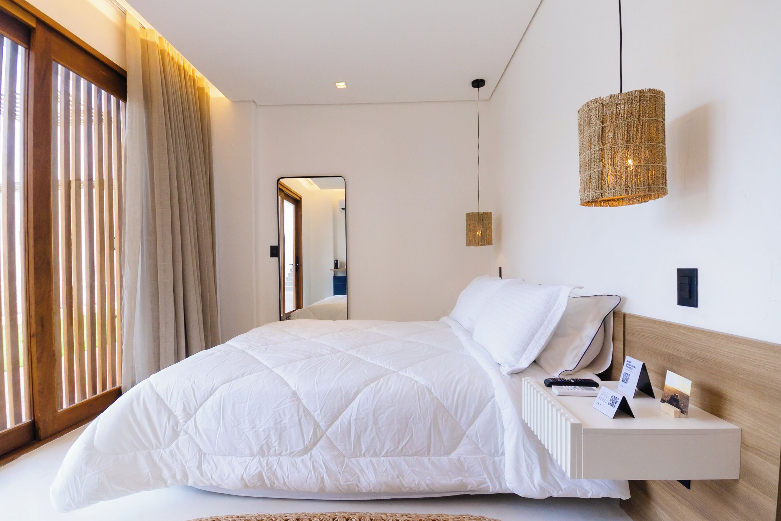 Un dormitorio moderno con una cama grande, mesitas de noche, una lámpara colgante y una ventana con persianas.