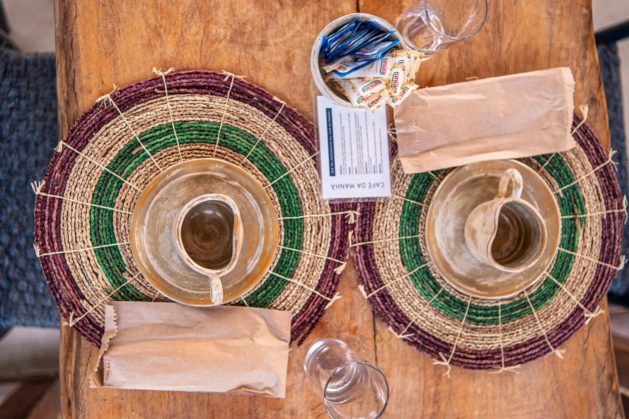 Dos posavasos tejidos con una etiqueta, un vaso y una bolsa de papel sobre una superficie de madera.