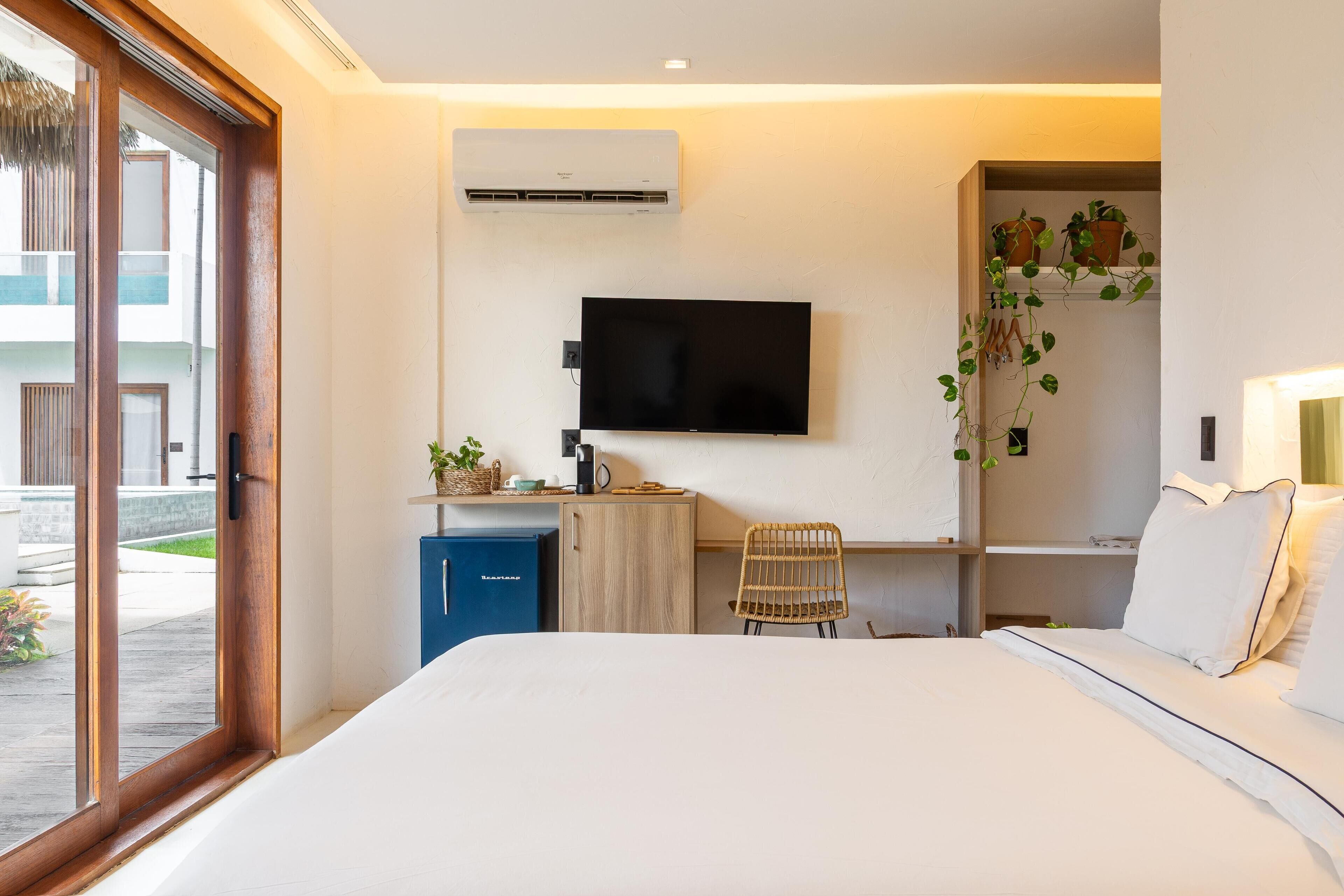 Habitación de hotel con cama, escritorio, silla, televisión, minibar y ventana con vistas al exterior.