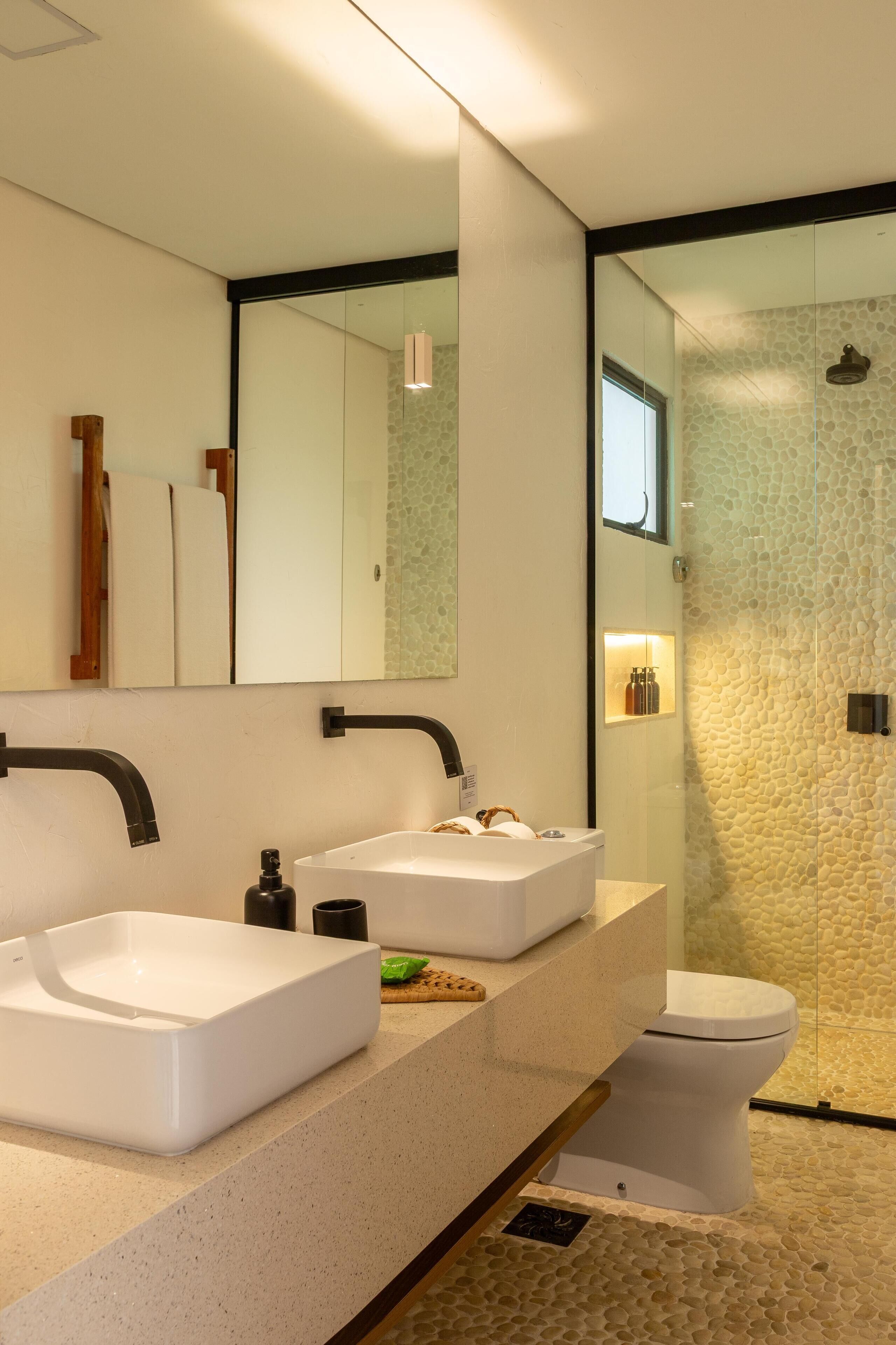 A modern bathroom with a large mirror, two sinks, a toilet, and a glass shower enclosure.
