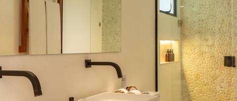 A modern bathroom with a large mirror, two sinks, a toilet, and a glass shower enclosure.