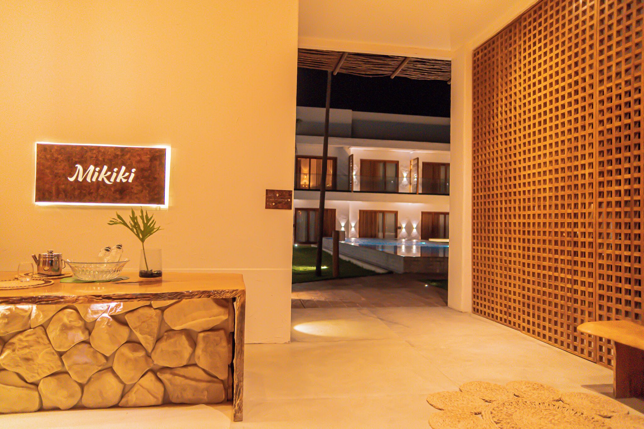 A reception area with a stone wall, a sign reading "Miki", a reception desk, and a view of a pool area.