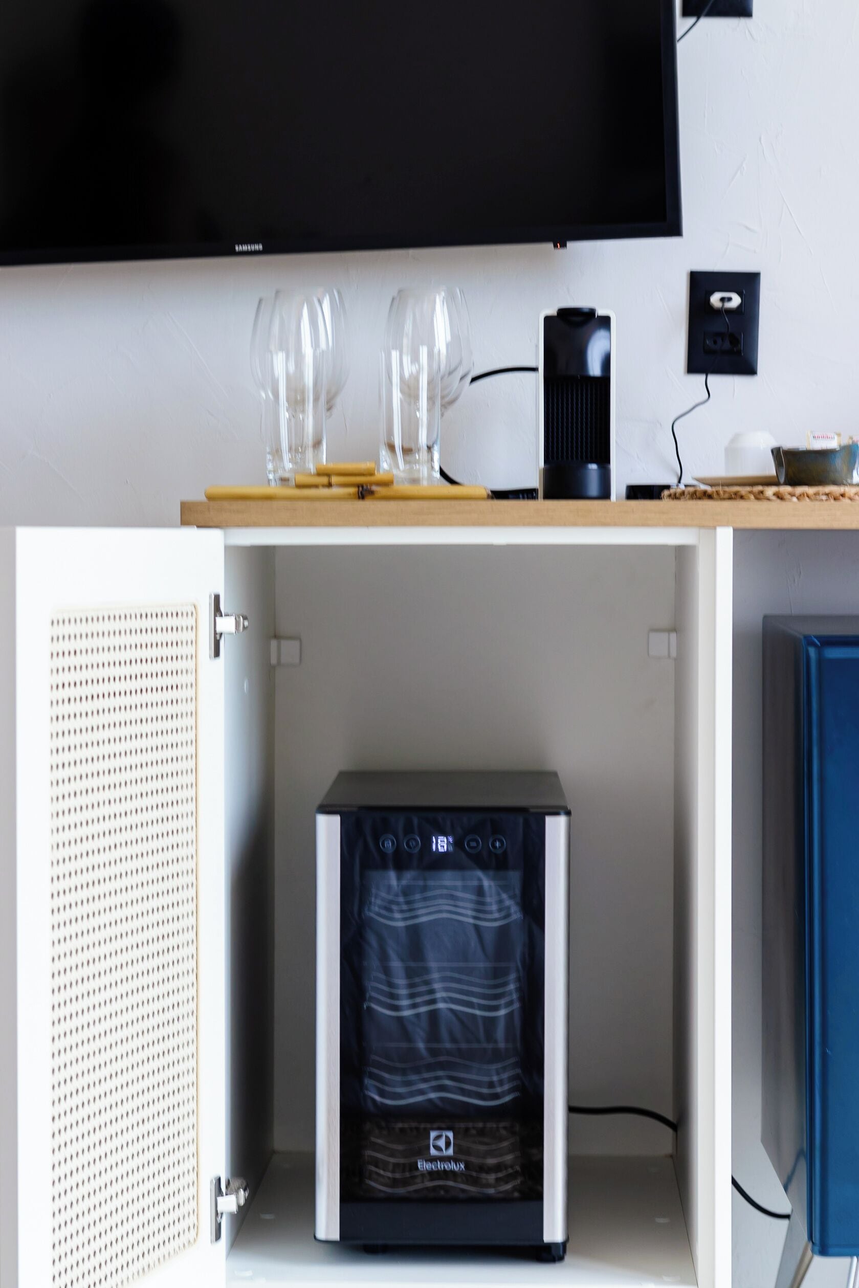 Habitación con televisión de pantalla plana en la pared, un mueble pequeño con microondas y un refrigerador.