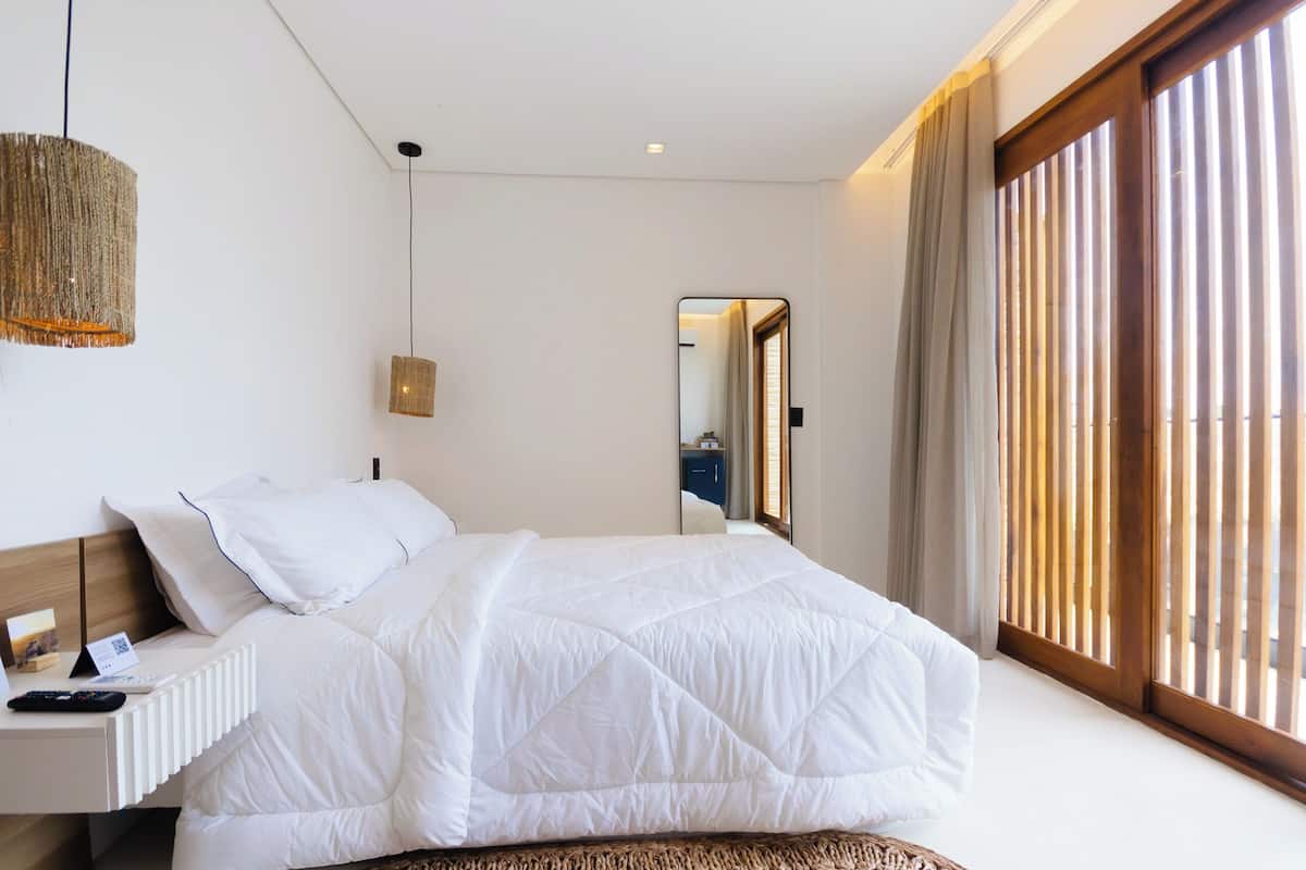 A modern bedroom with a large bed, a bedside table with a lamp, and a view of the outside through a sliding door.