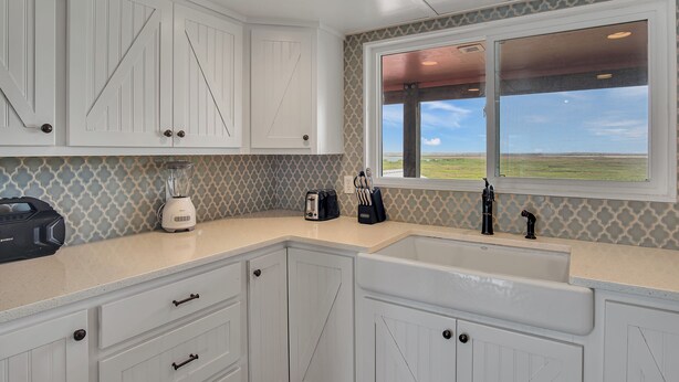A kitchen with white cabinetry, a countertop, a window with a view, and a built-in sink. - Beachin' Country by Silver Sands Vacation Rentals (Port Aransas)