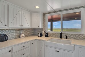 A kitchen with white cabinetry, a countertop, a window with a view, and a built-in sink. - Beachin' Country by Silver Sands Vacation Rentals (Port Aransas)