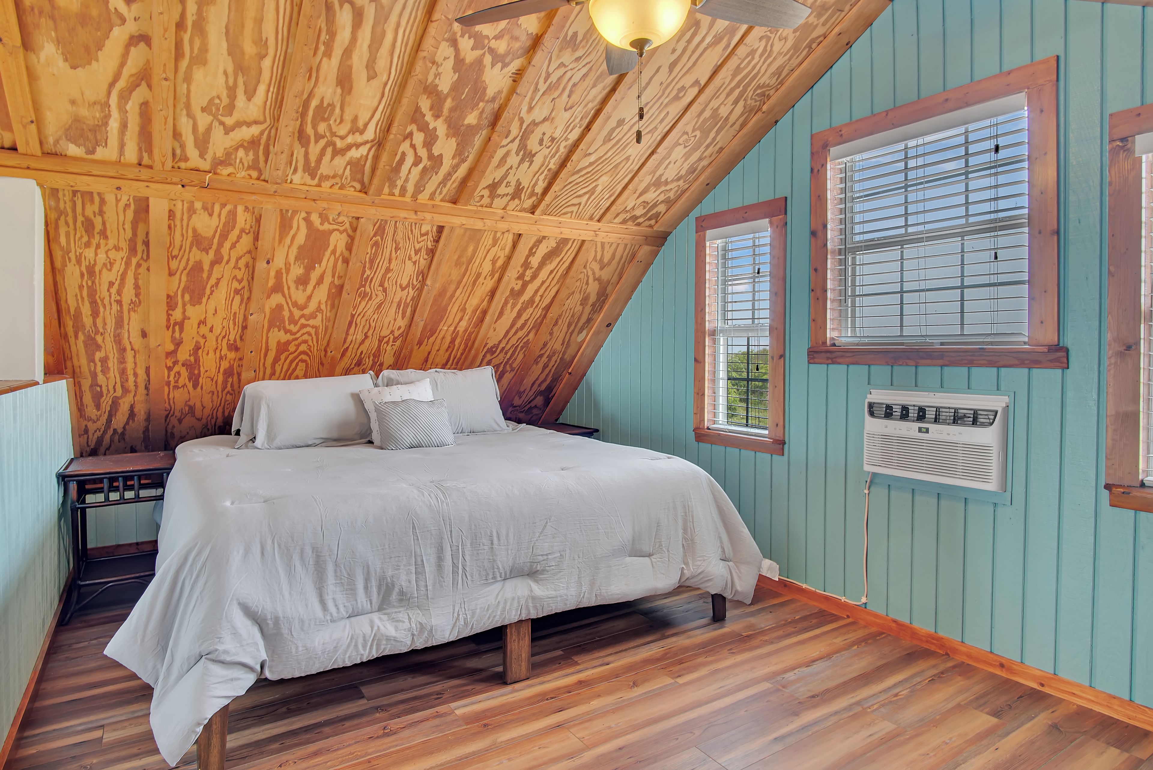 A bedroom with a wooden ceiling, a bed with white bedding, a nightstand, and a window with blinds.