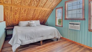 A bedroom with a wooden ceiling, a bed with white bedding, a nightstand, and a window with blinds. - Beachin' Country by Silver Sands Vacation Rentals (Port Aransas)