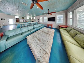 A spacious living area with a long light blue sofa, a green sofa, a wooden coffee table, and a ceiling fan.