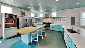 Een moderne keuken met een centraal eiland, roestvrijstalen apparatuur, blauwgroene kastjes en een blauwe vloer.
