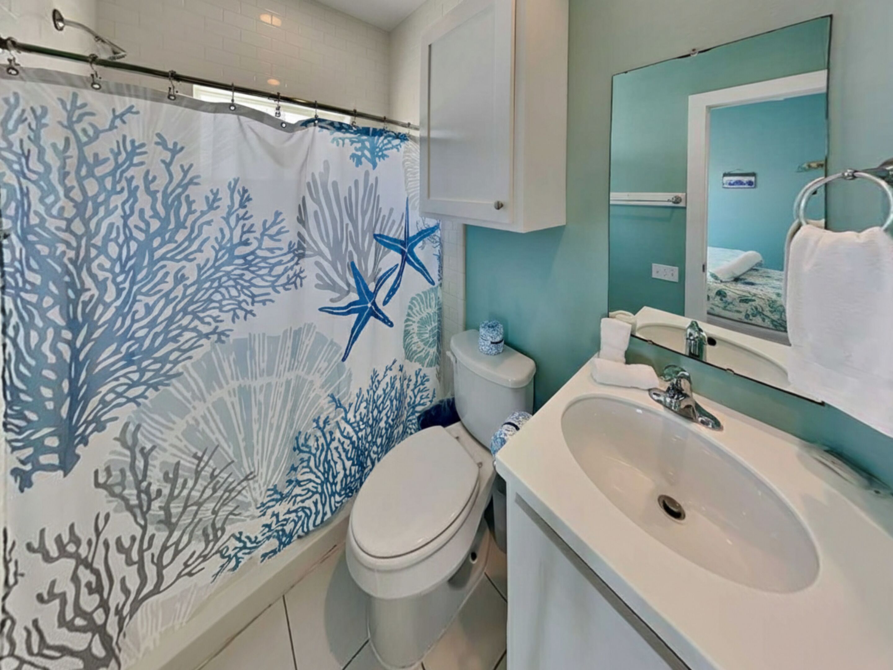 A bathroom with a shower curtain featuring a coral reef design, a toilet, a sink, and a mirror.