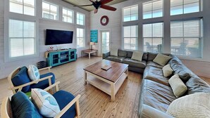 A spacious living room with a wooden floor, a large leather sofa, a wooden coffee table, and a television. - Bella Vista by Silver Sands Vacation Rentals (Port Aransas)